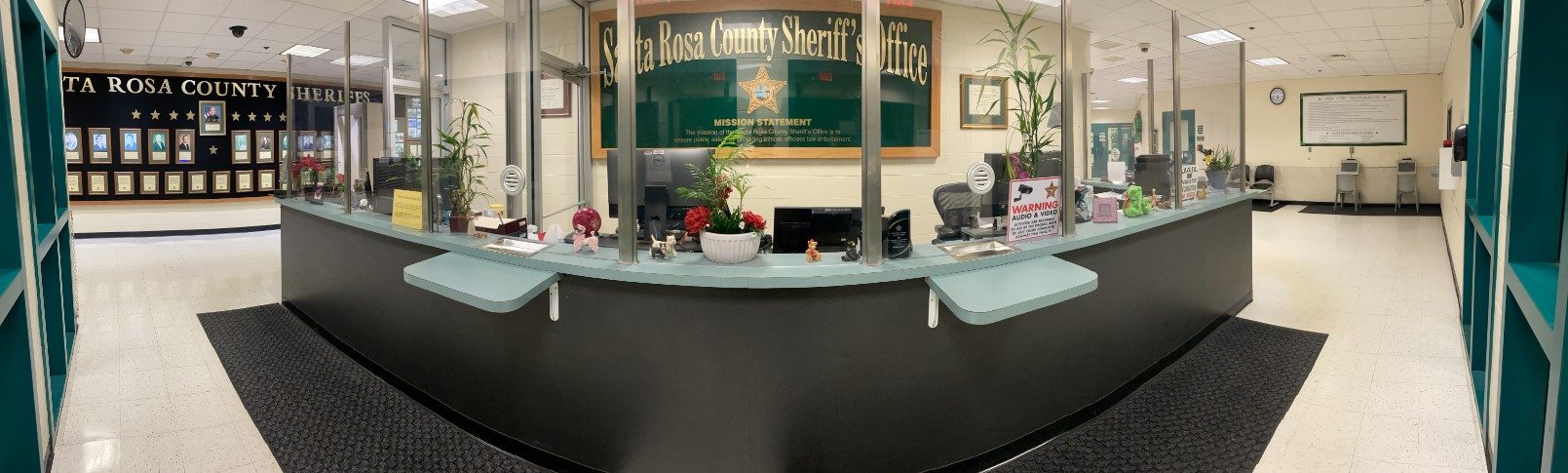 Interior view of the santa rosa county sheriff's office reception area with a curved counter, informational signs, and decorations.