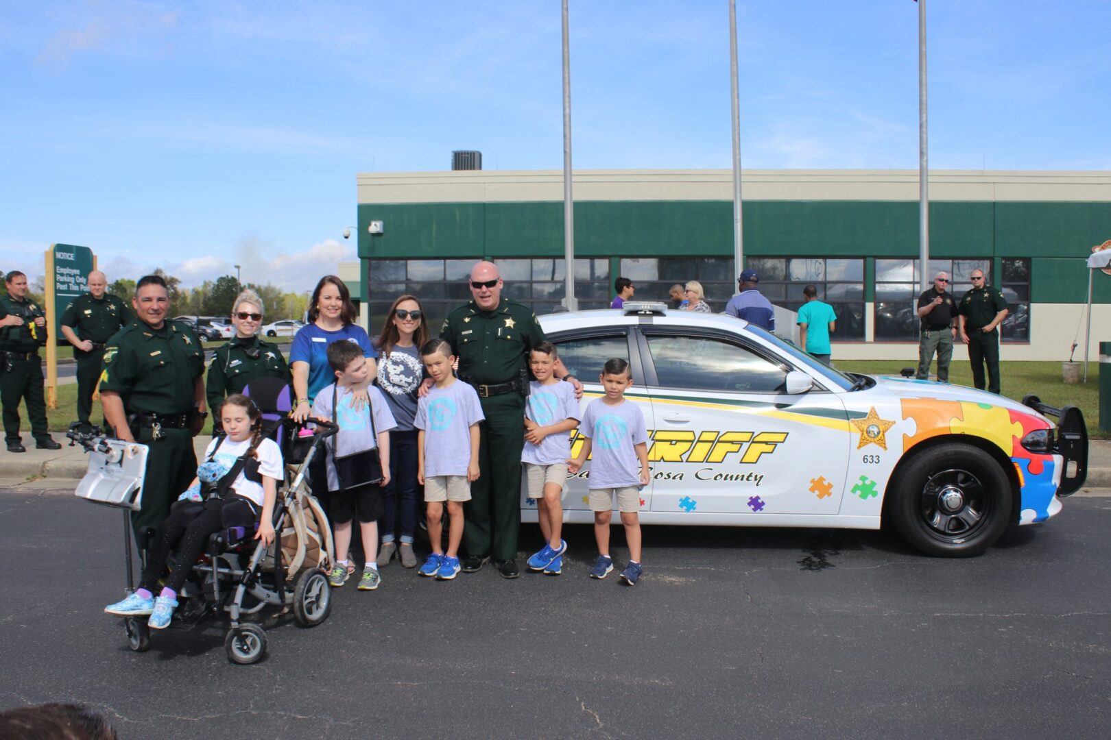 Group of people, including children and adults, posing with a sheriff's car at a community event.