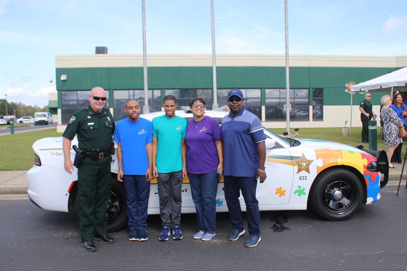 Two police officers and four civilians standing beside a police car at a community event.