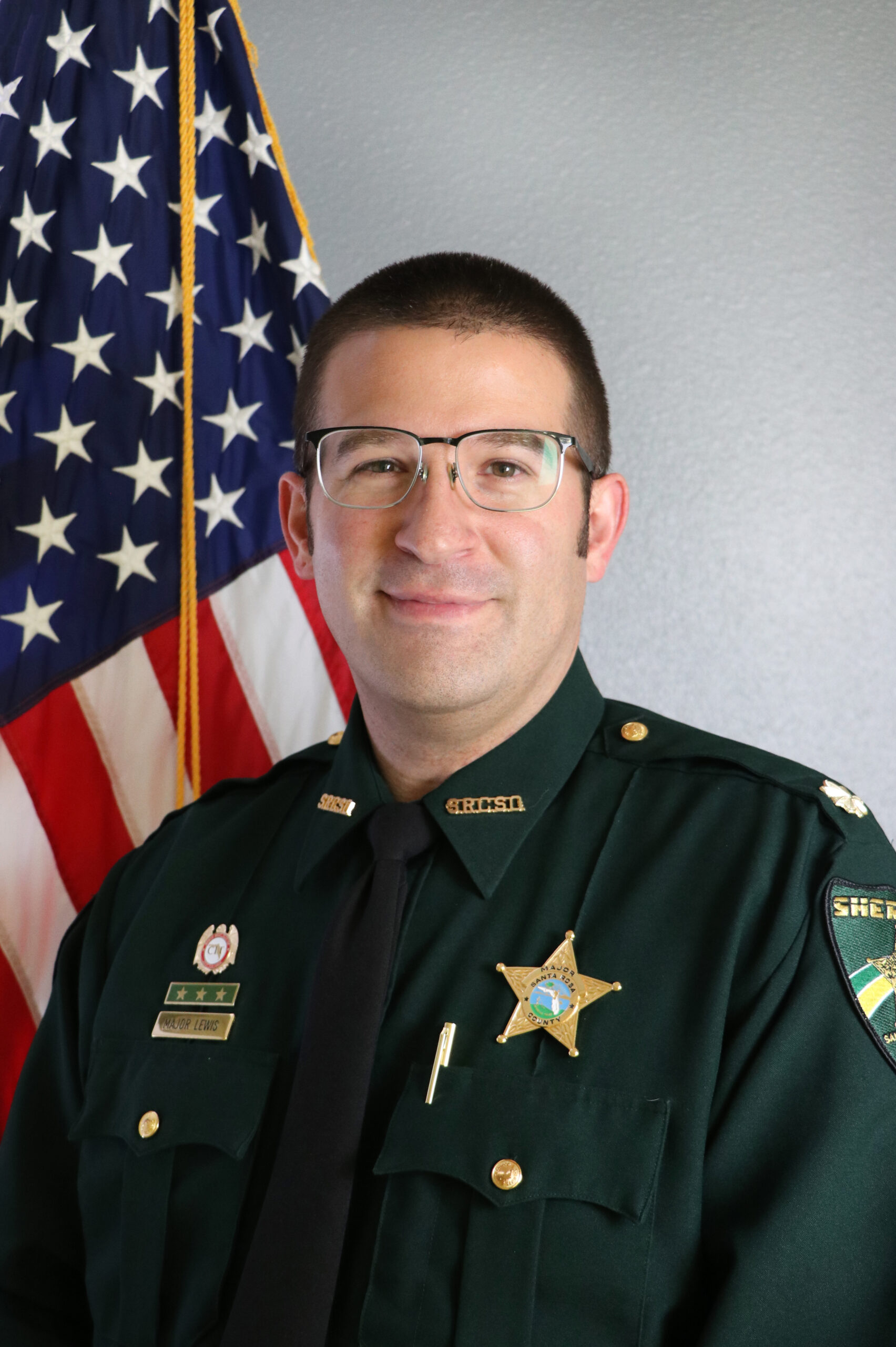 A smiling sheriff's deputy in uniform, standing in front of an american flag.