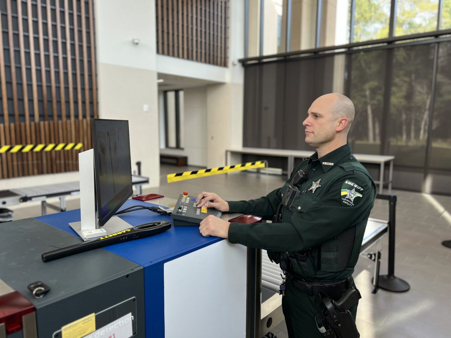A sheriff's deputy operating a security console in a modern building lobby.