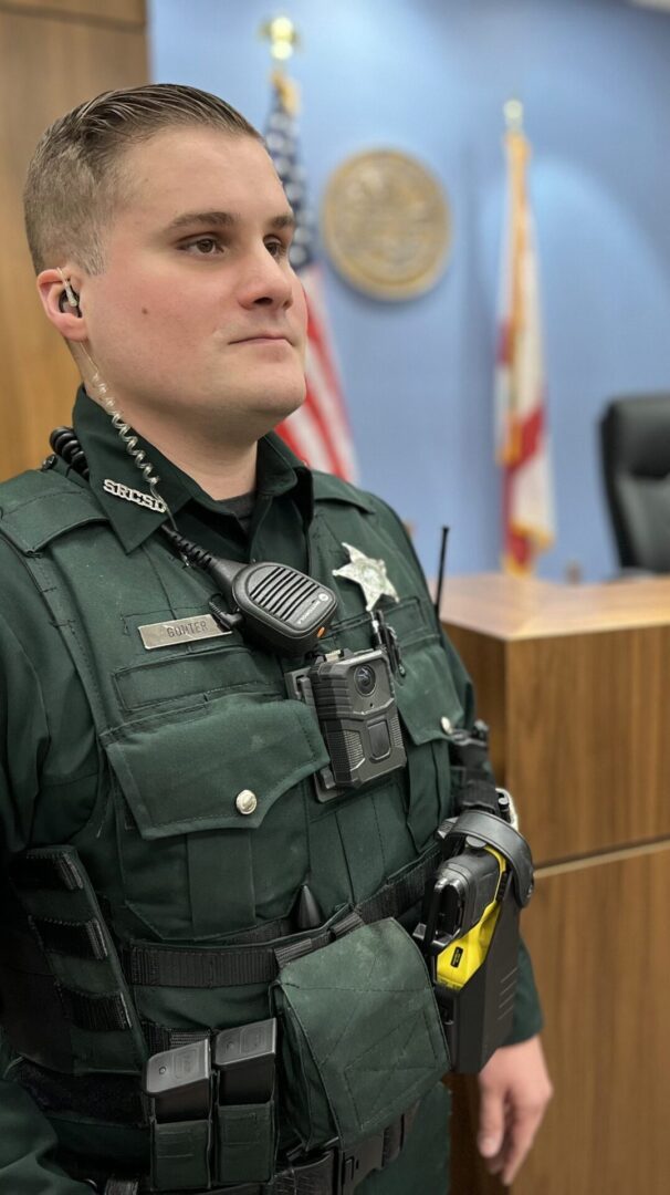 A close-up of a male sheriff officer in uniform, standing in a courtroom, with a focused expression.