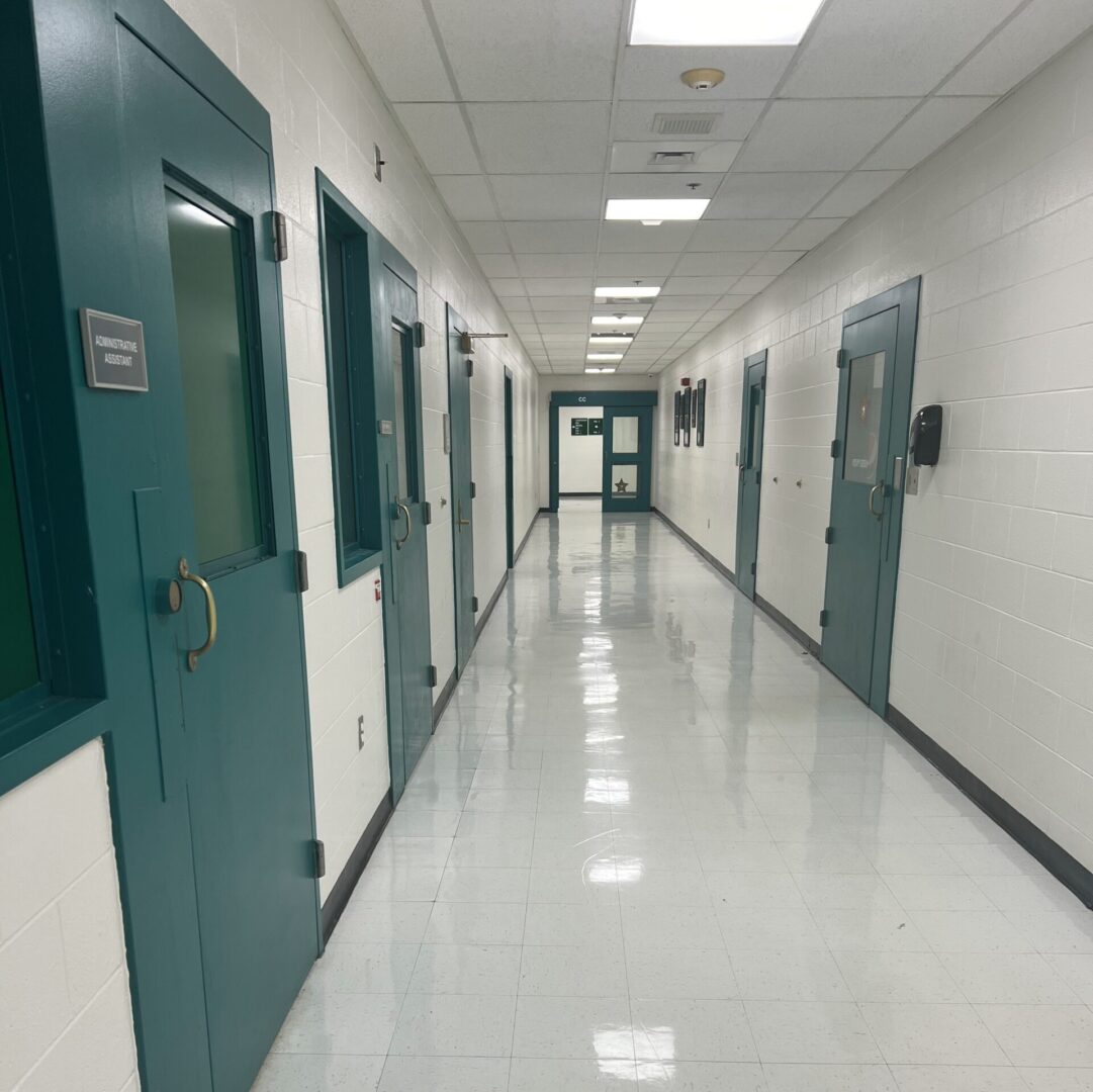 A brightly lit school hallway with shiny tiled floors and green doors on either side.
