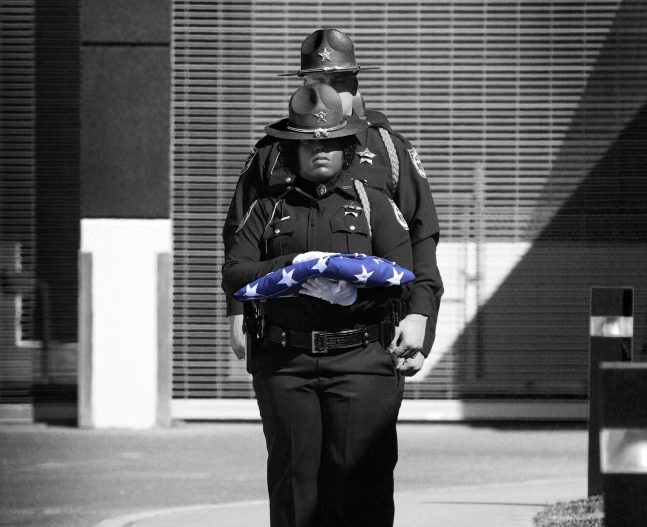 A police officer in uniform solemnly carrying a folded american flag.